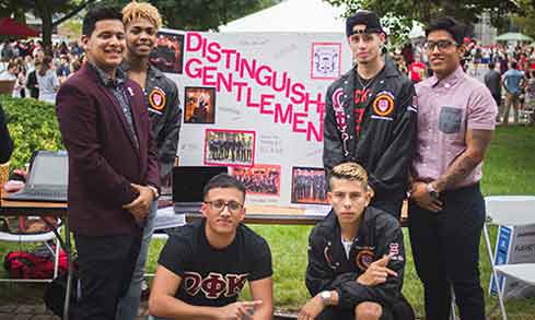 A group of young men smiling and posing together for a photo at a lively event.