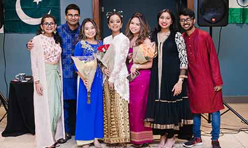 A group of people smiling and posing together in front of a large flag.