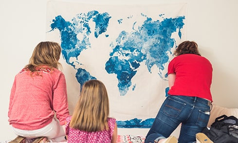 Students hang a tapestry on a dorm room wall.