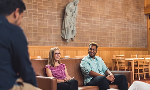 Students sit in front of a brick wall.