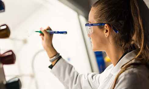 A student wearing a lab coat and safety glasses holds up a marker.