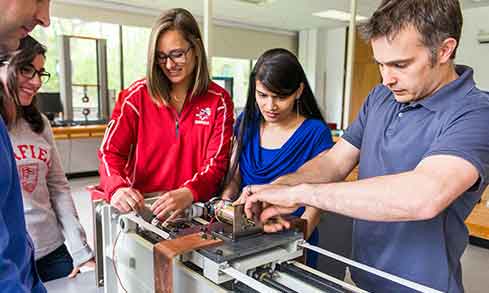 Five students work together at a piece of machinery