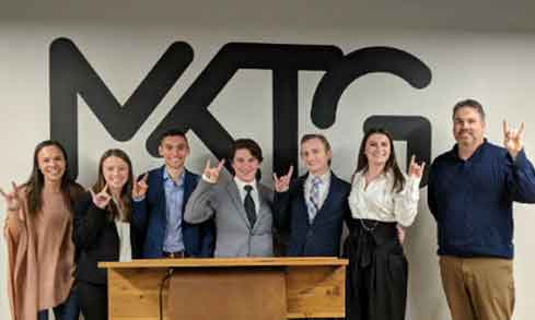 A group of 7 student interns pose with their hands in the "Stag" symbol