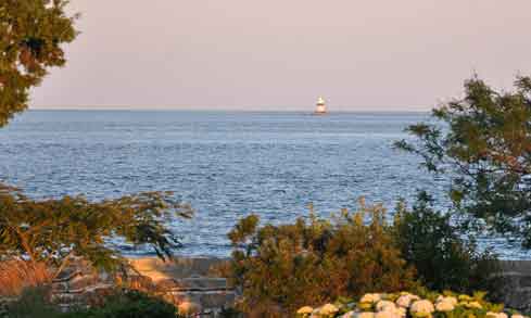 A lighthouse is far in the distance with blue water and a purple sky.