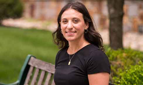 A student in a black shirt smiles on a bench outdoors