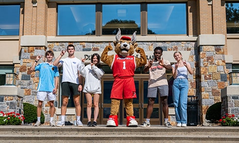 Students standing and posing excitedly with Fairfield's mascot, Lucas the Stag, on the steps of the Library.