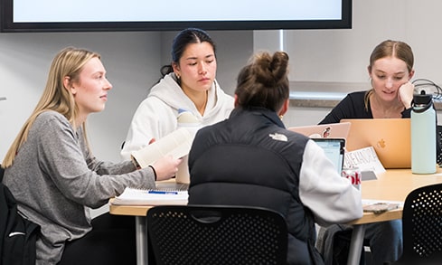 Four students sit and work collaboratively at a study room table.