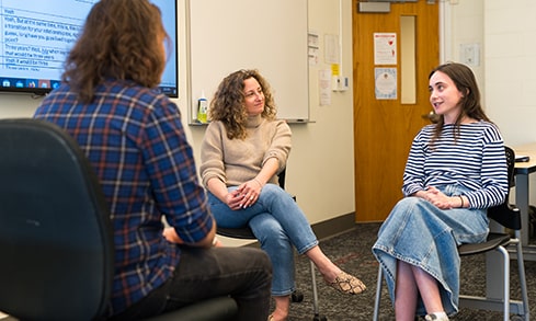 Two students sit across from a third as they engage in conversation with one another.