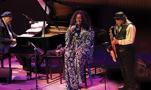 Woman sitting and singing on stage behind band.