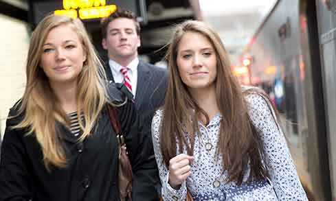 A group of three students walk next to a train, dressed for work