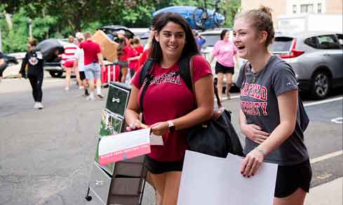 Two students carry bags into their residence hall on move in day.