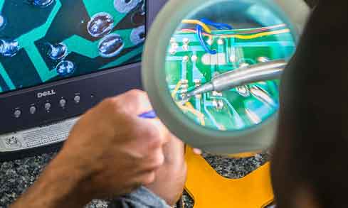 A student uses a magnifying glass to look at a computer chip.