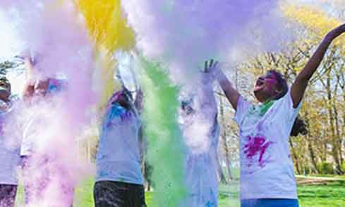 Students wearing white t-shirts throwing up powdered paint. 