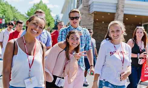 Large group of students walking through campus wearing lanyards. 