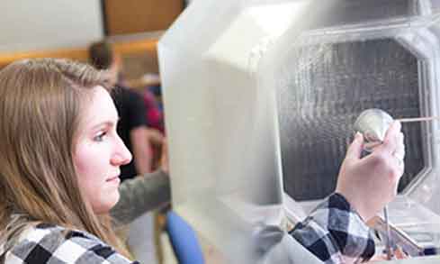 A student looks at an electrical device in a glass case.