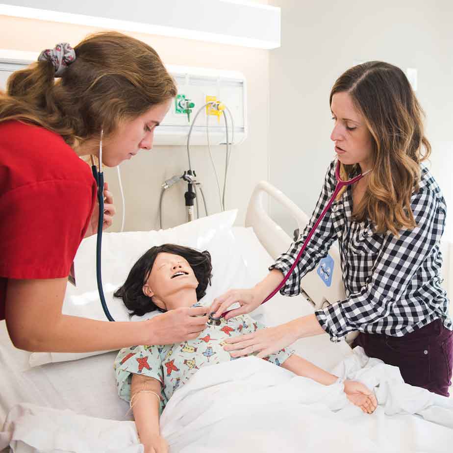 A woman closely examines a simulation doll placed in a hospital bed.