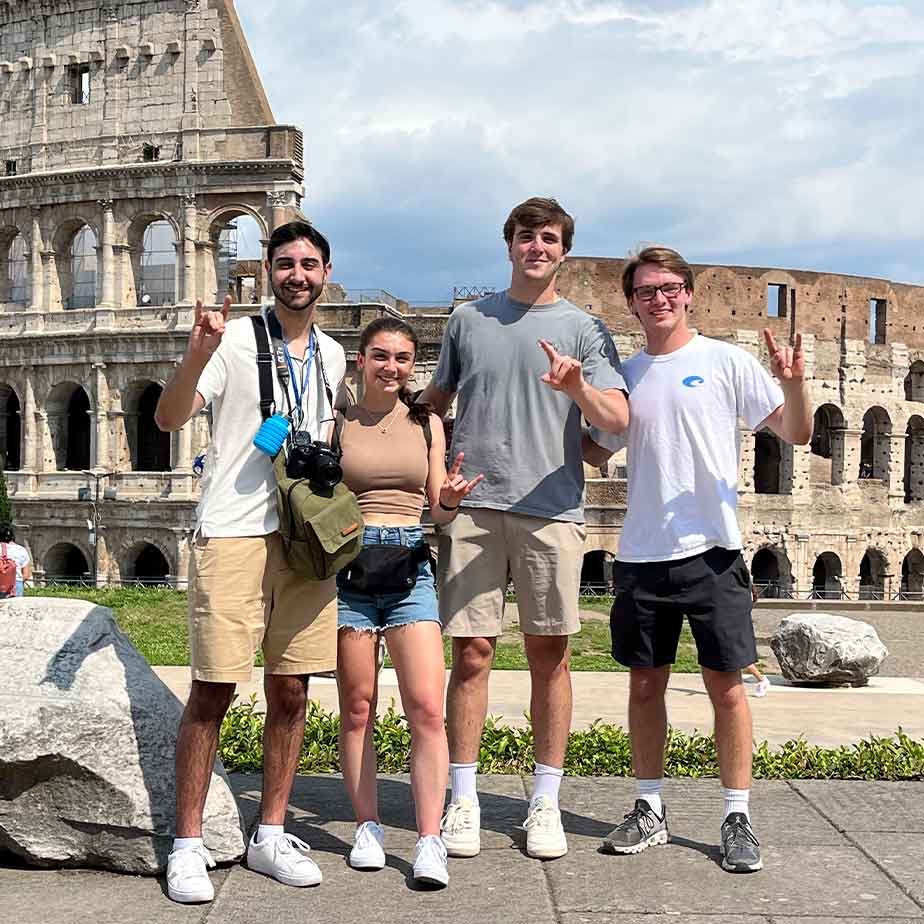 Four individuals smiling together in front of the Colosseum, capturing a memorable moment at the historic landmark.