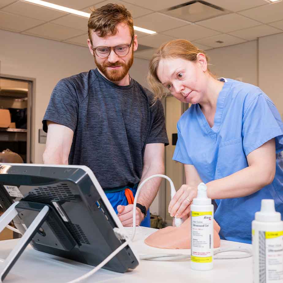  man and woman in scrubs collaborate on a computer, focused on their work in a professional healthcare setting.