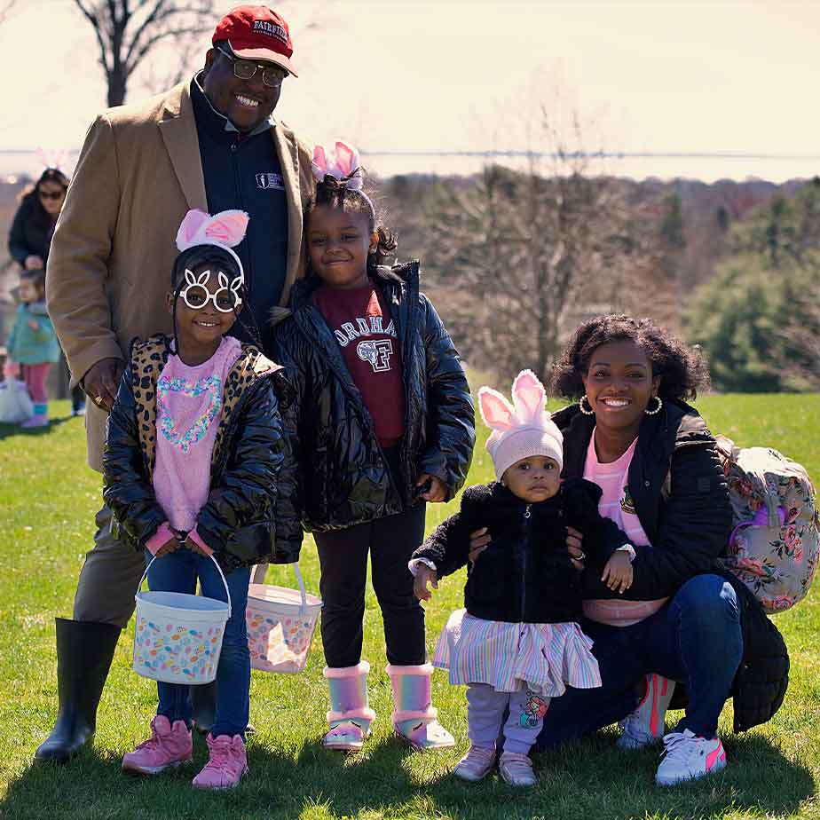 A family smiles for a photo in front of a colorful field filled with Easter eggs, celebrating the holiday together.