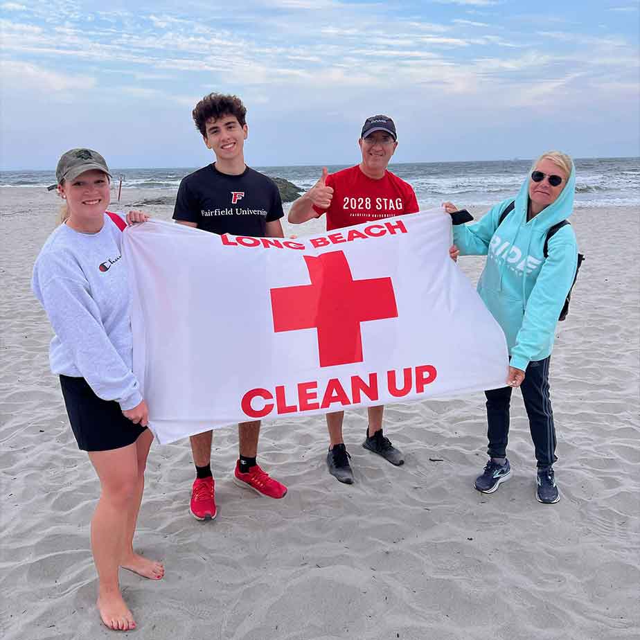 Four individuals hold a red cross clean-up sign while working together on a beach to promote environmental awareness.