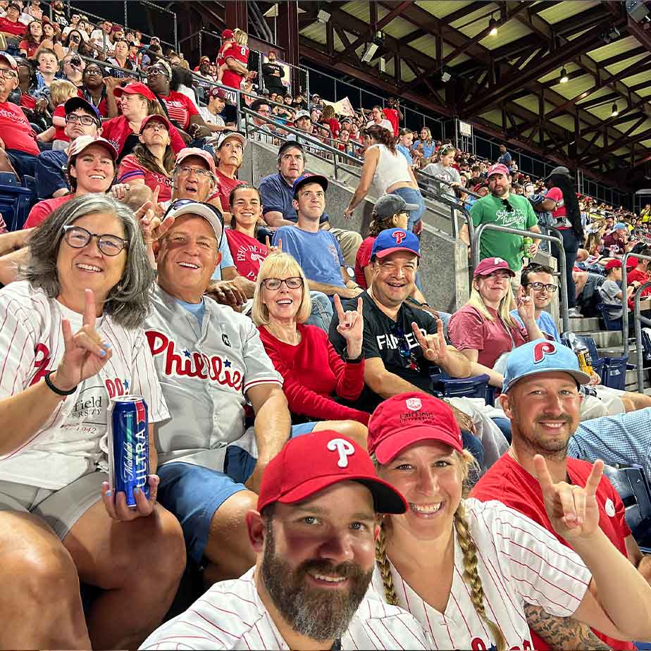 A group of alumni at a baseball game wearing Phillies hats and shirts.