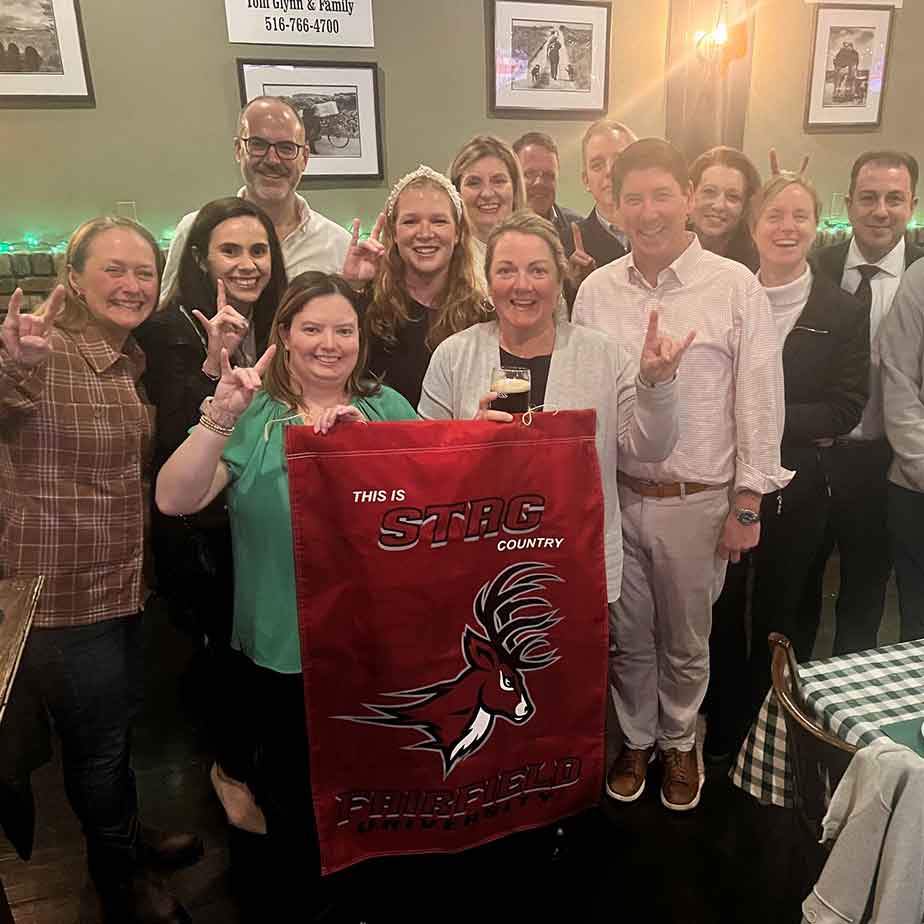 A large group in a restaurant holds up a newsflag and smiles.