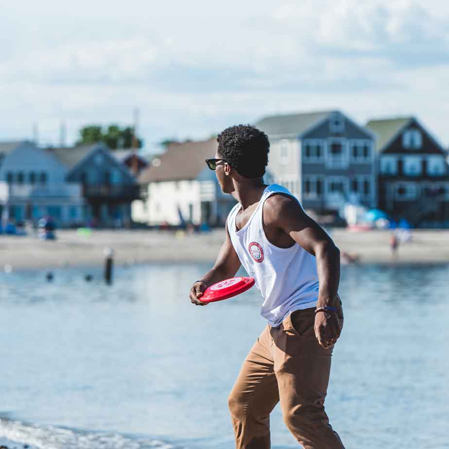 A man in a white tank top throws a frisbee, showcasing an active outdoor scene.