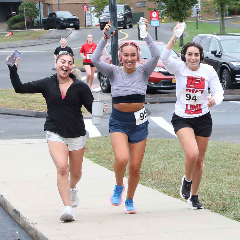 Three women compete in a race, with one of them holding a water bottle as they sprint towards the finish line.