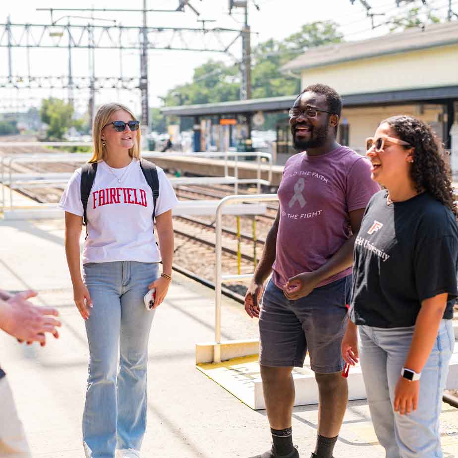 A group of students engaged in conversation with a man on a train platform, surrounded by a bustling travel atmosphere.