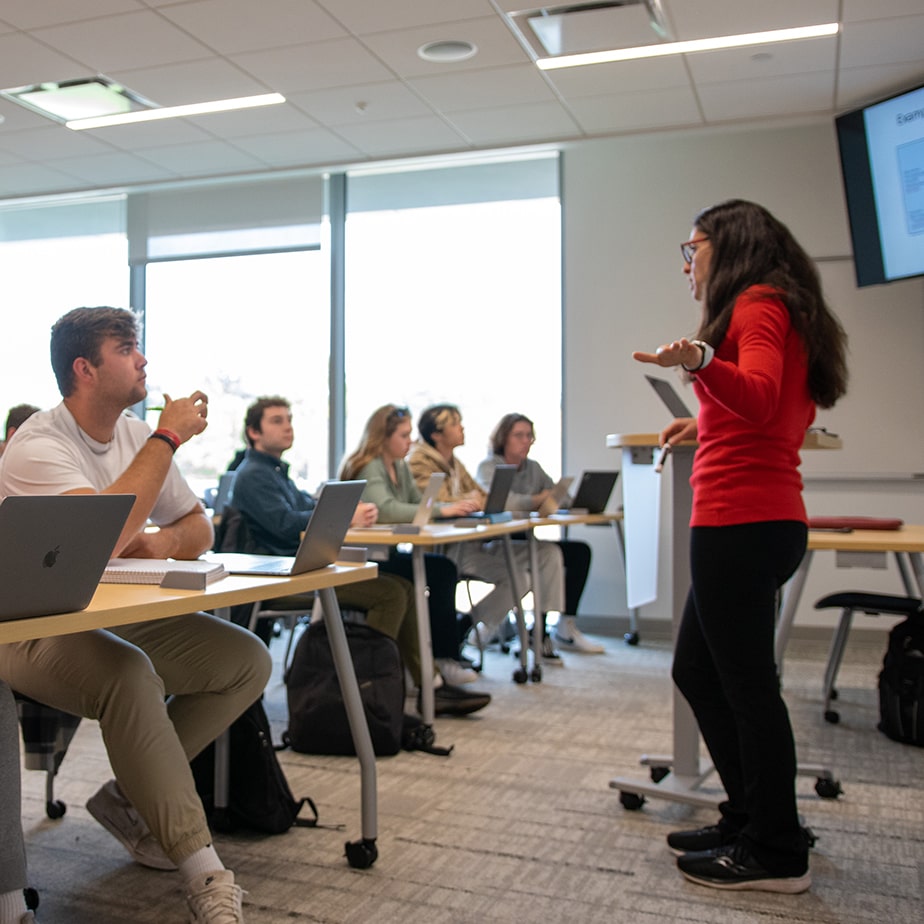 Students sitting in class listening to their professor give a lecture at the front of the classroom. 