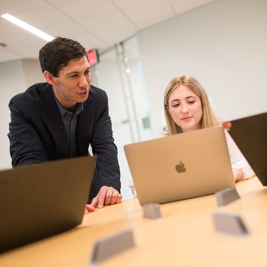 Students wearing formal attire sitting with their laptops receiving feedback from their professor. 