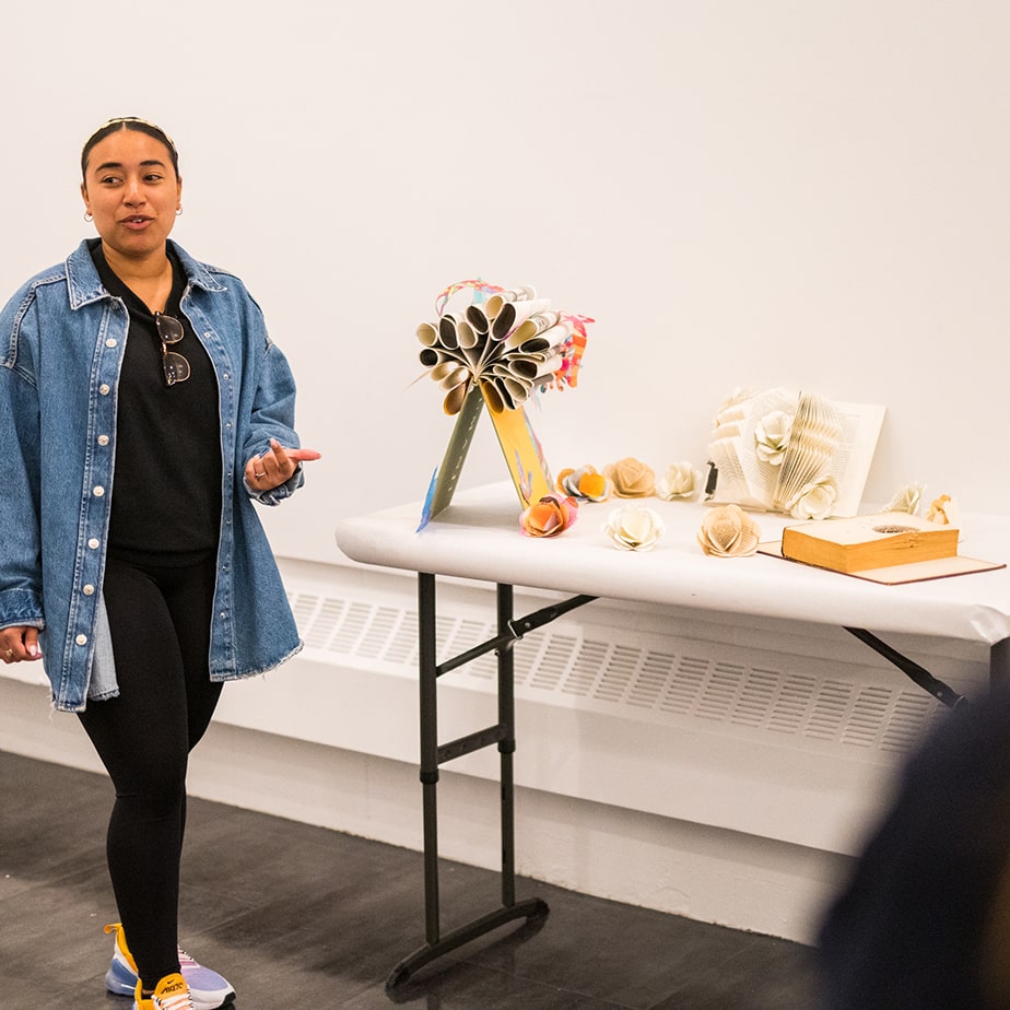 Student wearing denim gives a presentation on artwork.