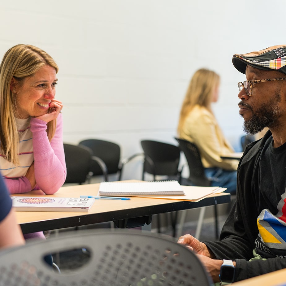 Two students talking to each other at a table. 