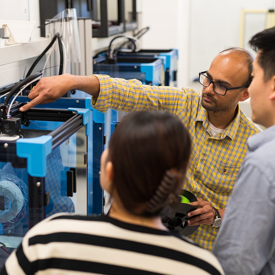 Professor pointing to something on machine while two students watch. 