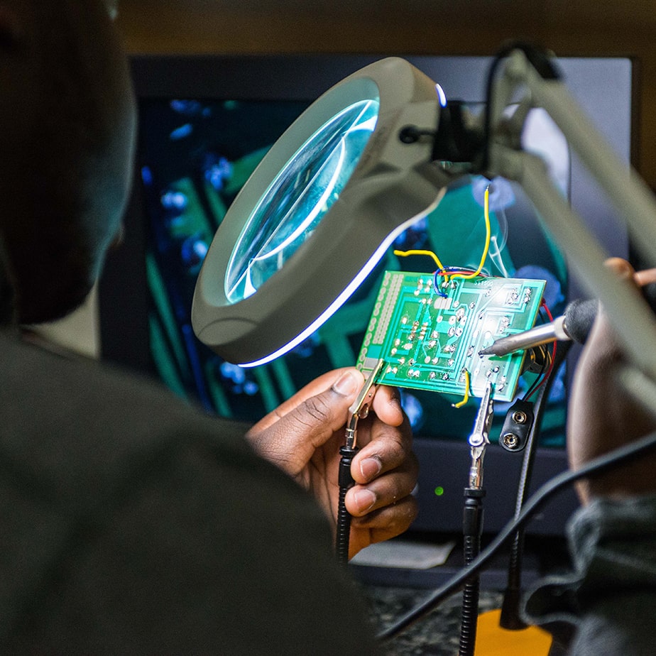 Professor examines a microchip underneath a magnifying instrument. 