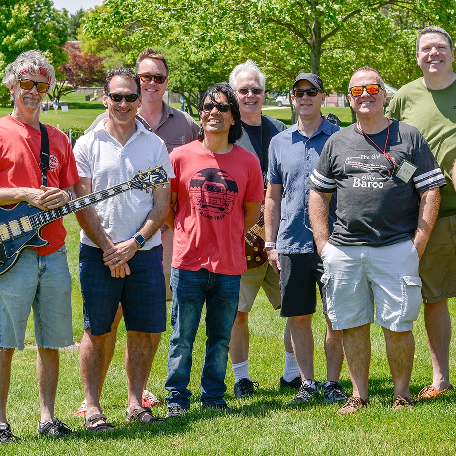 A group of alumni smile for a photo with some holding guitars.