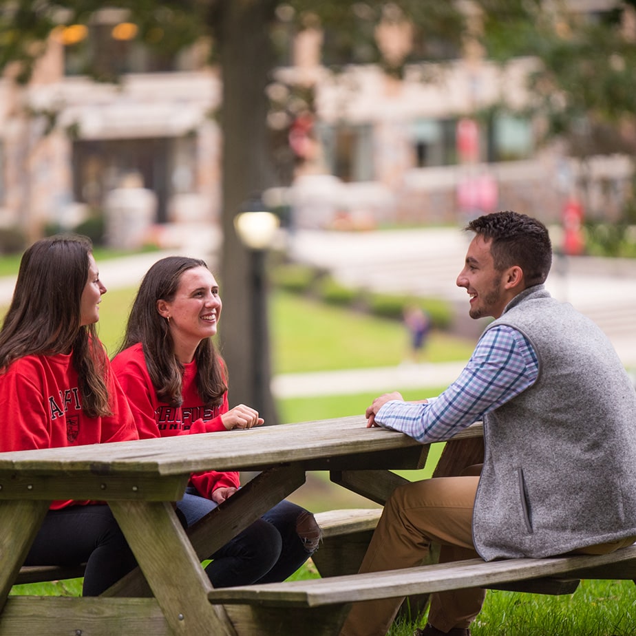 Students sitting and talking at a picnic table outside on campus.