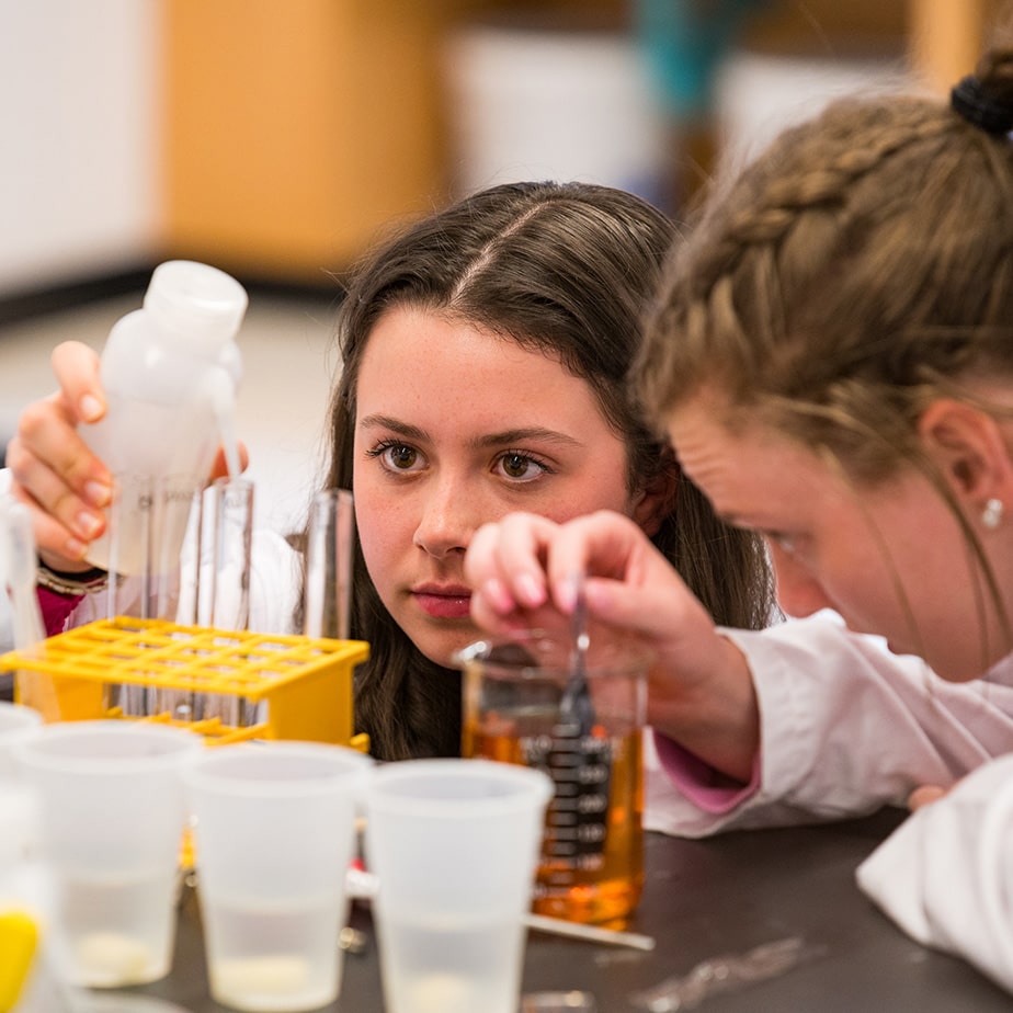 Students kneel down at the workstation and delicately move liquids from one container to another.