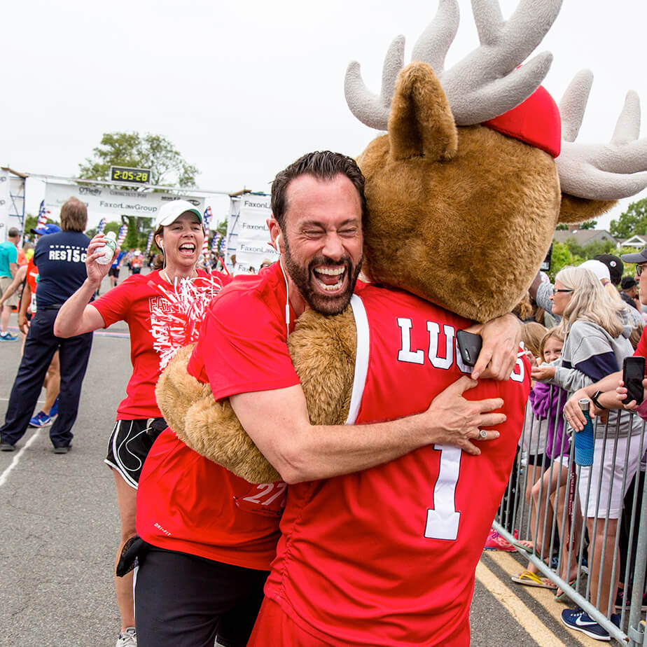 A man joyfully embraces a Lucas the mascot, at the annual Fairfield Half Marathon.