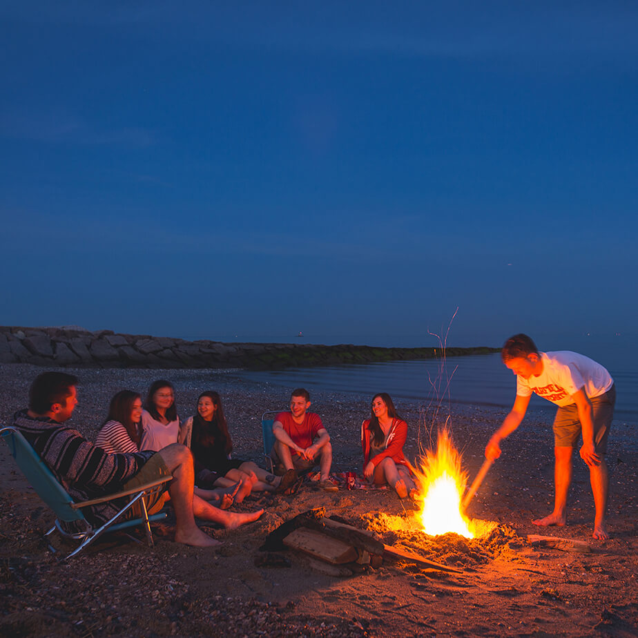 A circle of friends around a beach fire, creating a cozy atmosphere as they relax and converse under the stars.