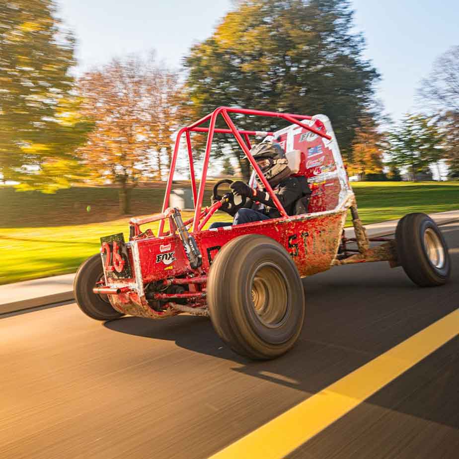 A red car drives down a road with a side that reads “Stags”.