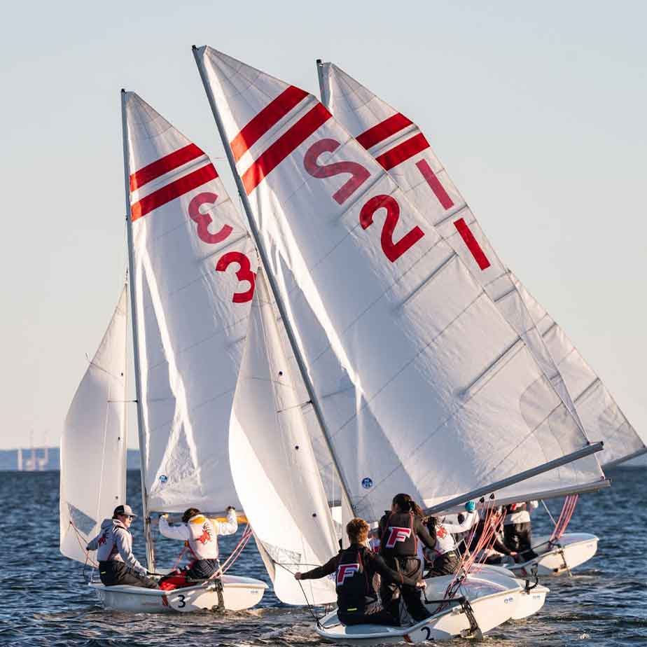 People on three sailboats in the water.