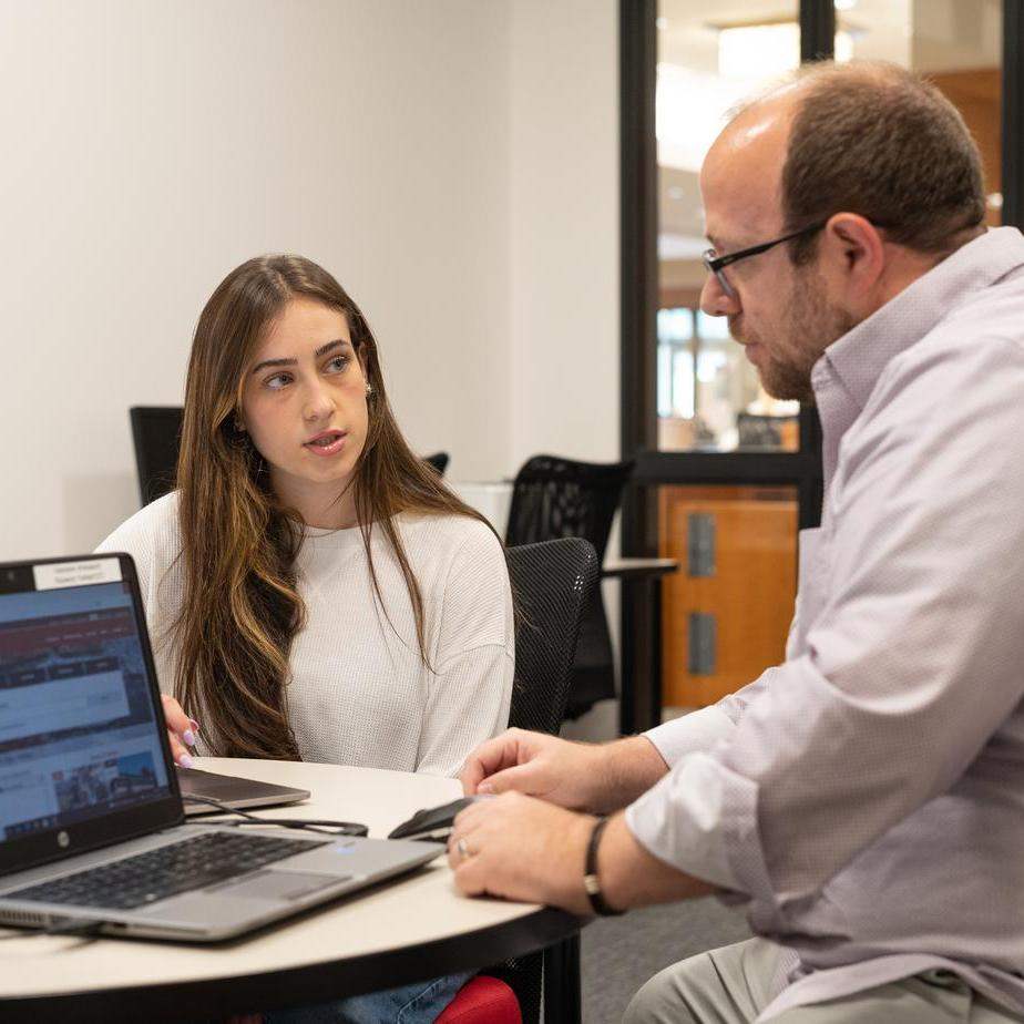 A student talks with an advisor at a table in the library