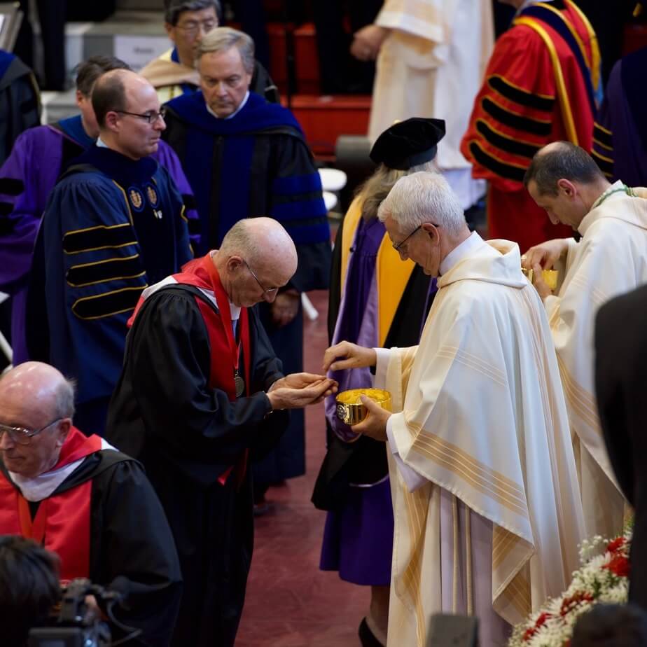 A group of alumni receive the eucharist from a priest.