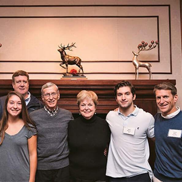 A group of people, smile in front of a mantle decorated by three stag statues.