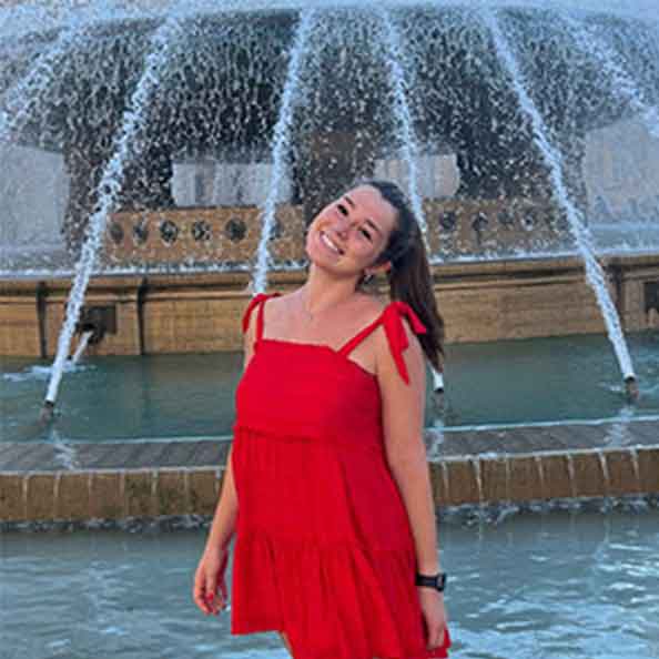 Abigail Grenier smiles in a red dress in front of a fountain.