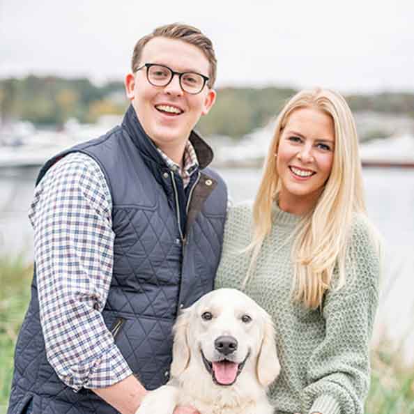 Two people smile with a golden retriever below them.