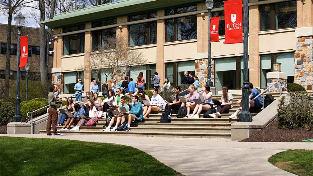 Student sitting on library steps listening to a professor on a beautiful sunny day.