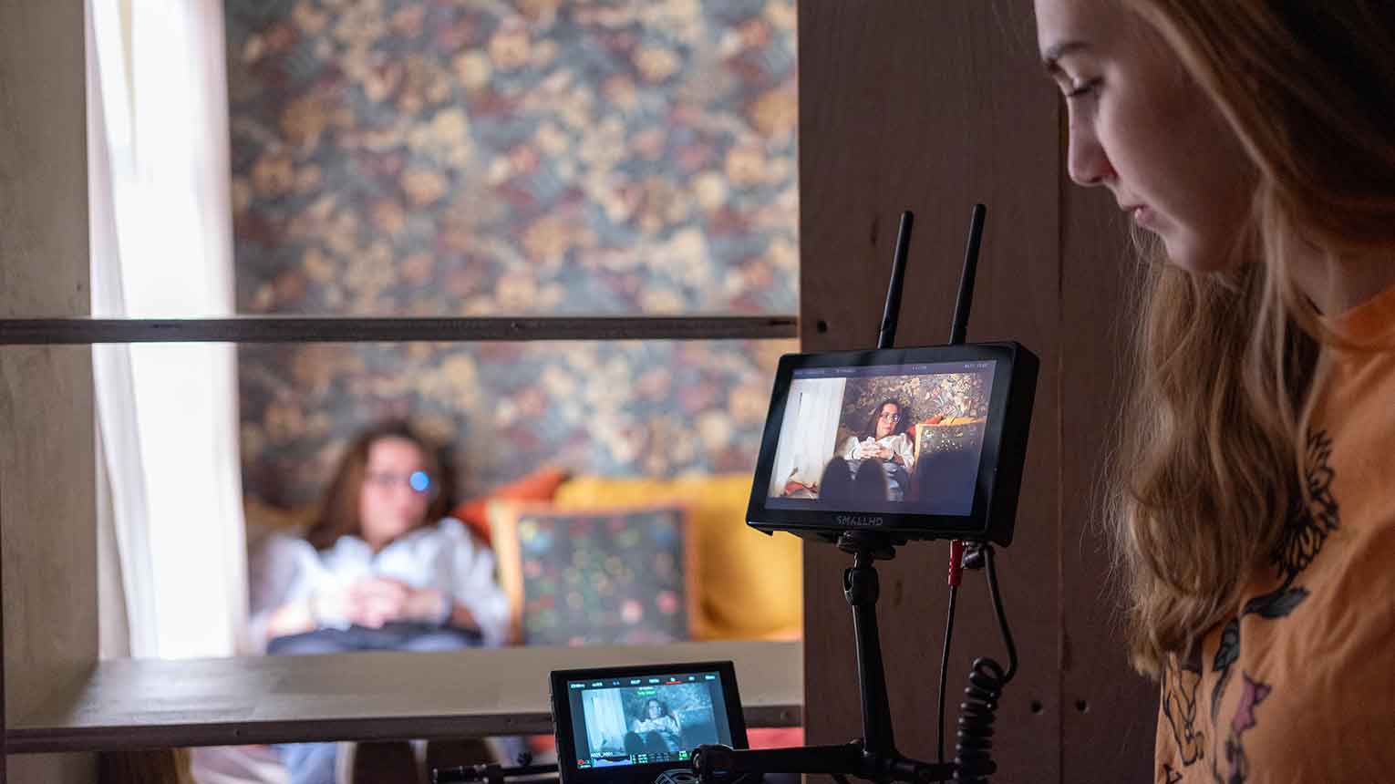 A woman works a camera while filming an actor on set.