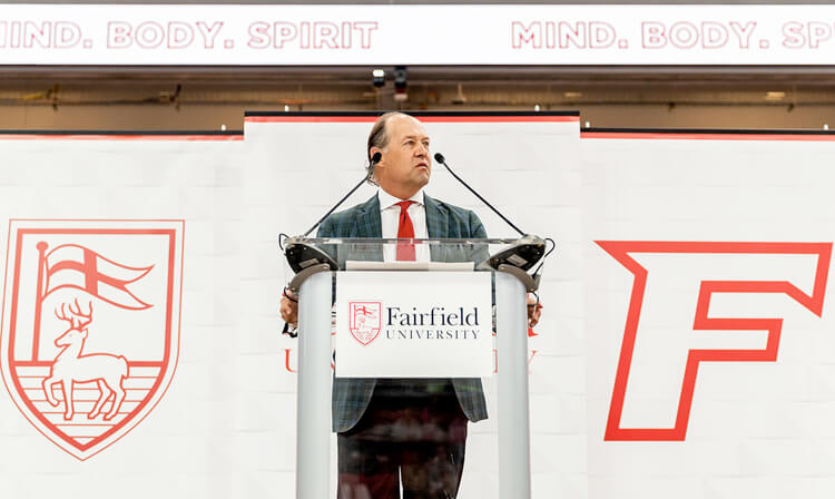 President Nemec in a suit and tie stands at a podium, preparing to deliver a speech to an attentive audience.